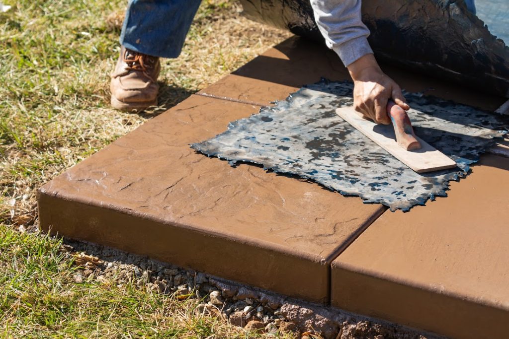 A worker applying pressure to a texture template on wet cement.